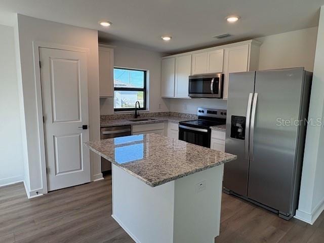 kitchen with sink, appliances with stainless steel finishes, a center island, light stone counters, and white cabinets