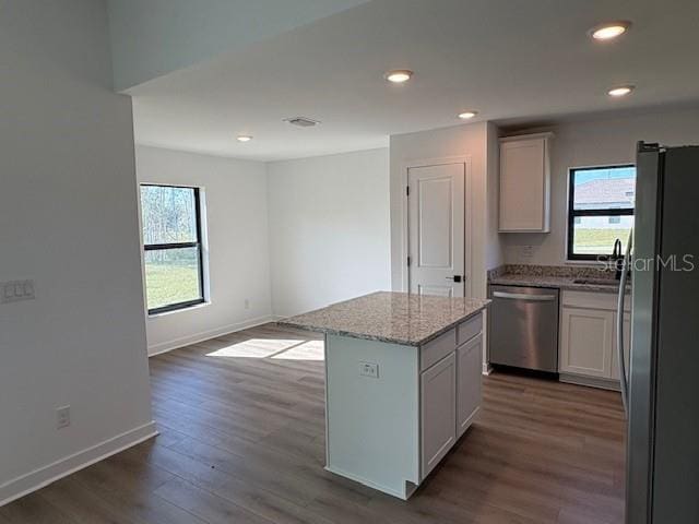 kitchen with light stone counters, a center island, dark hardwood / wood-style flooring, stainless steel appliances, and white cabinets