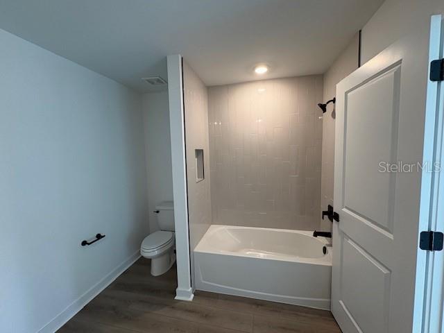 bathroom with shower / washtub combination, toilet, and hardwood / wood-style floors