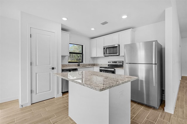 kitchen with light stone counters, visible vents, wood finish floors, a kitchen island, and stainless steel appliances