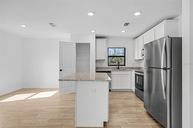 kitchen with a sink, stainless steel appliances, wood finish floors, visible vents, and a center island