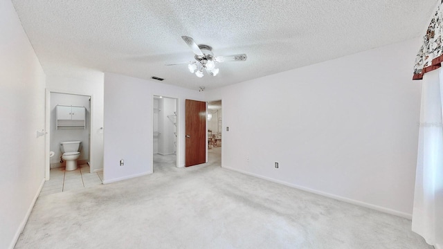 unfurnished bedroom with ceiling fan, ensuite bath, light carpet, and a walk in closet