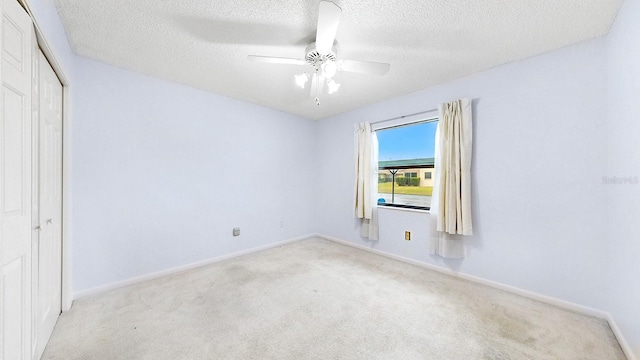 unfurnished bedroom with a textured ceiling, light colored carpet, a closet, and ceiling fan