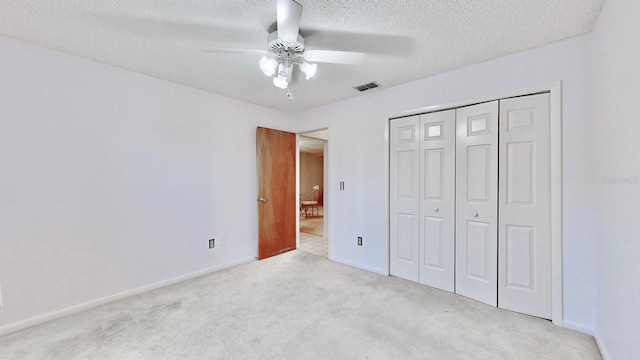 unfurnished bedroom with ceiling fan, light colored carpet, a closet, and a textured ceiling