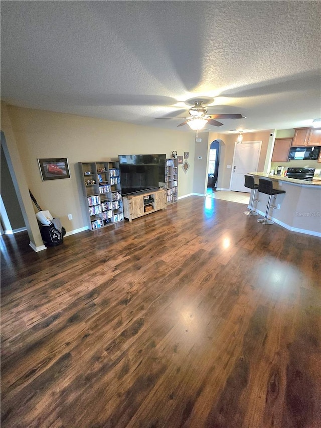 unfurnished living room with dark wood-style floors, a textured ceiling, baseboards, and a ceiling fan