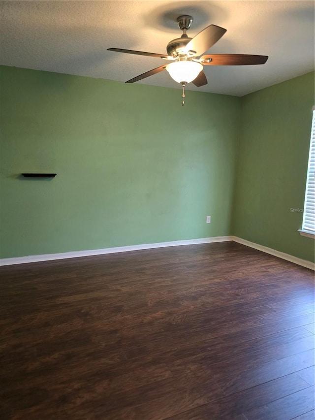 empty room with a textured ceiling, ceiling fan, dark wood-type flooring, and baseboards