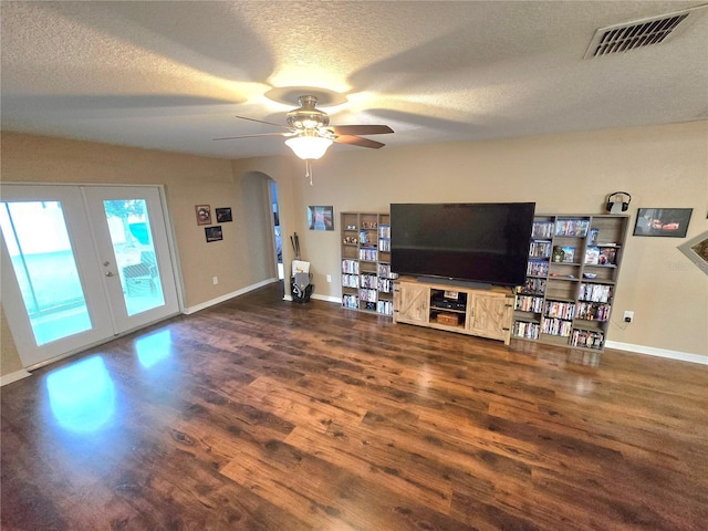 living area featuring arched walkways, visible vents, dark wood-type flooring, a textured ceiling, and baseboards