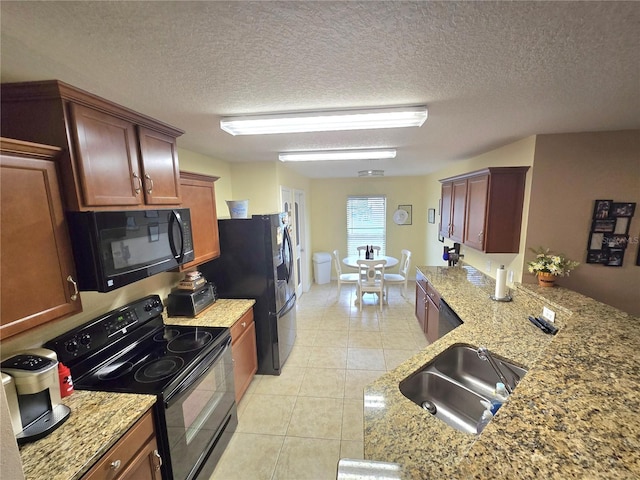 kitchen with light tile patterned floors, light stone counters, a textured ceiling, black appliances, and a sink