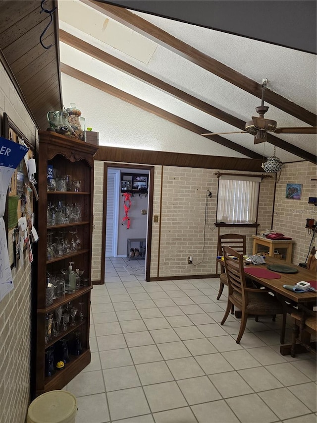 tiled dining space featuring ceiling fan, lofted ceiling with beams, a textured ceiling, and brick wall