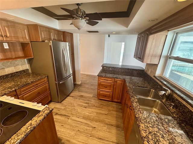 kitchen featuring sink, stainless steel fridge, a tray ceiling, light hardwood / wood-style floors, and decorative backsplash