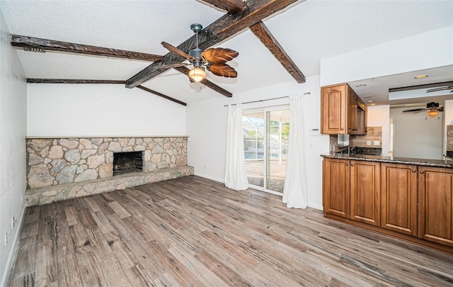 unfurnished living room featuring a fireplace, lofted ceiling with beams, light hardwood / wood-style floors, and ceiling fan