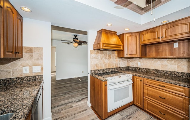 kitchen featuring ceiling fan, light hardwood / wood-style floors, custom range hood, oven, and dark stone counters