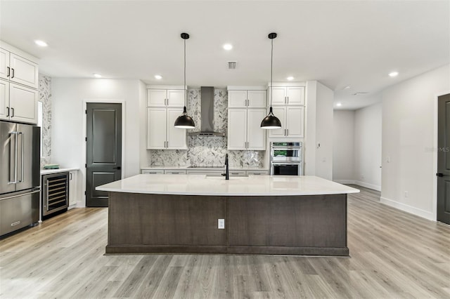 441 42nd Ave NE, Saint Petersburg, FL 33703 - kitchen with appliances with stainless steel finishes, wall chimney range hood, beverage cooler, decorative backsplash, and light wood-type flooring