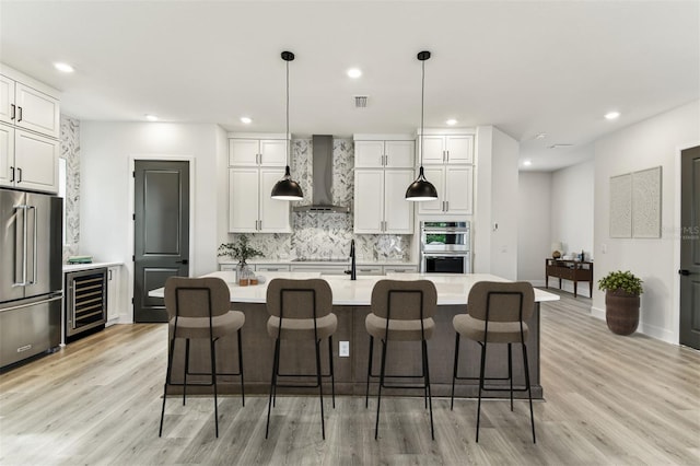441 42nd Ave NE, Saint Petersburg, FL 33703 - kitchen featuring appliances with stainless steel finishes, wall chimney range hood, beverage cooler, light wood finished floors, and tasteful backsplash