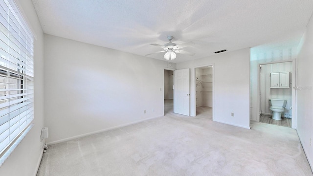 unfurnished bedroom with ensuite bath, ceiling fan, a textured ceiling, a walk in closet, and a closet