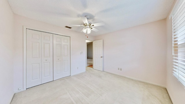 unfurnished bedroom featuring light colored carpet, a textured ceiling, ceiling fan, and a closet