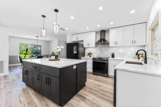 kitchen with decorative light fixtures, white cabinets, stainless steel range with electric cooktop, black fridge, and wall chimney exhaust hood