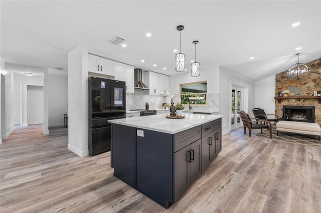 kitchen with wall chimney range hood, black refrigerator, white cabinets, vaulted ceiling, and light wood-type flooring