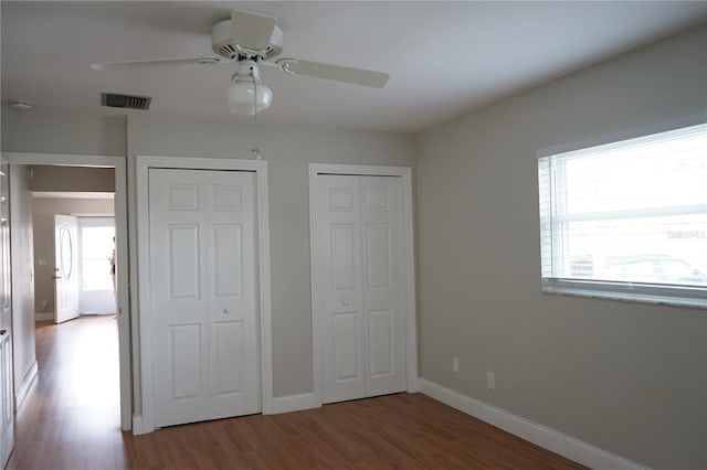 unfurnished bedroom with multiple closets, ceiling fan, and hardwood / wood-style floors