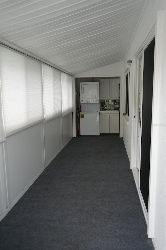 hall with stacked washer / dryer, vaulted ceiling, and dark carpet