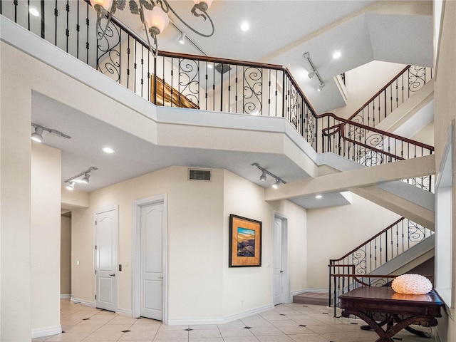 stairway featuring tile patterned flooring, a towering ceiling, and track lighting