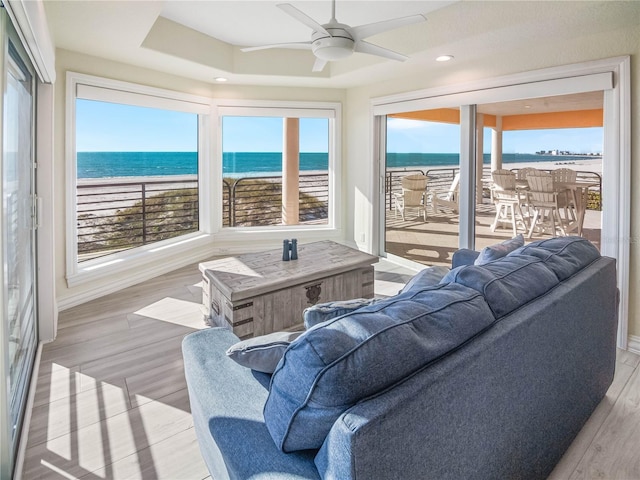 sunroom / solarium featuring a tray ceiling, ceiling fan, and a water view