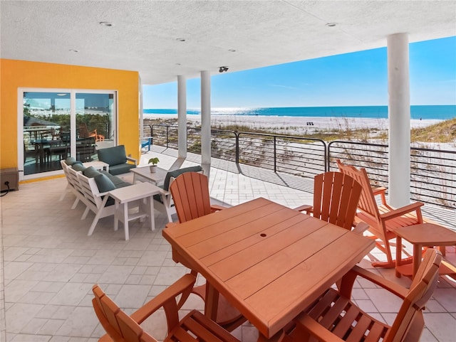 view of patio / terrace with a balcony, a water view, and a beach view