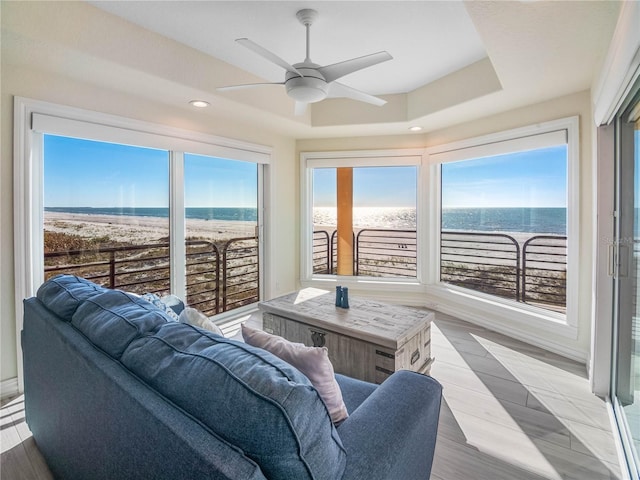 sunroom with a raised ceiling, ceiling fan, and a water view