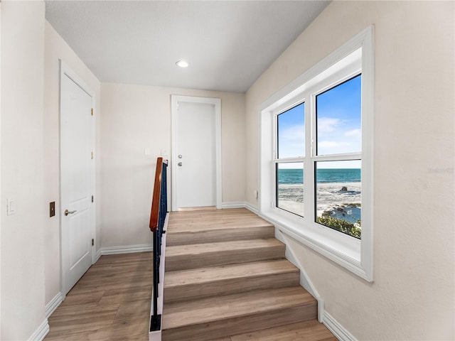 stairway featuring a view of the beach, wood-type flooring, and a water view