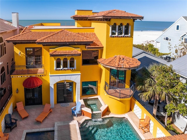 rear view of house with a patio area, an in ground hot tub, and a water view