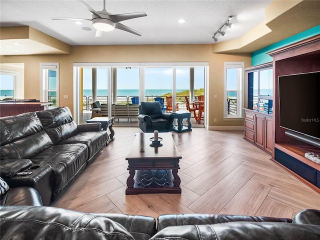 living room with light parquet flooring, rail lighting, ceiling fan, and a textured ceiling