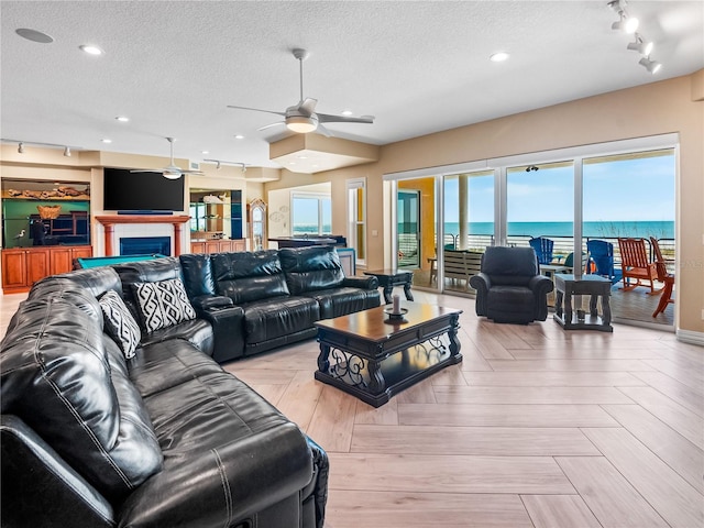 living room with ceiling fan, light parquet flooring, a water view, track lighting, and a textured ceiling