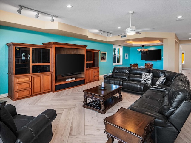 living room with ceiling fan with notable chandelier, a raised ceiling, and a textured ceiling