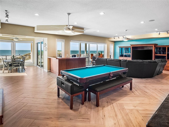 recreation room with a water view, ceiling fan, light parquet flooring, and a textured ceiling