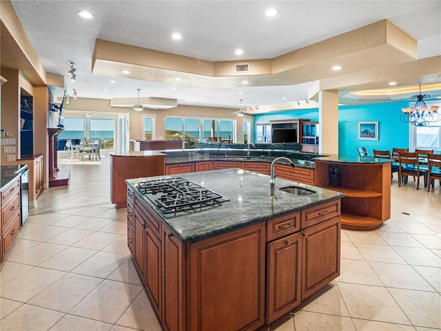 kitchen with a large island, sink, dark stone counters, and stainless steel gas stovetop