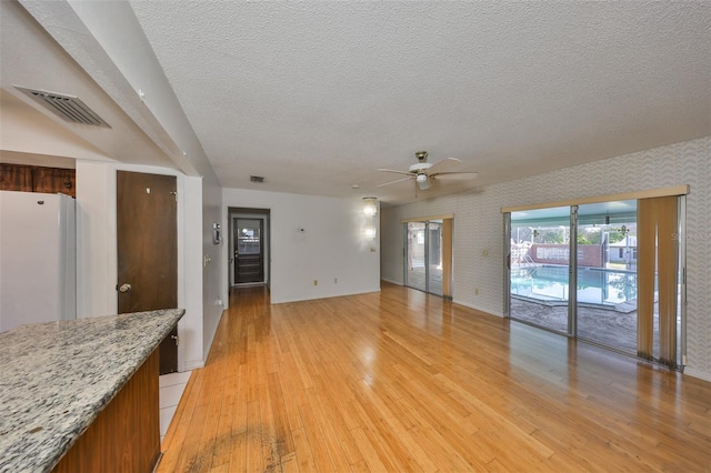 unfurnished living room featuring ceiling fan, a textured ceiling, and light wood-type flooring