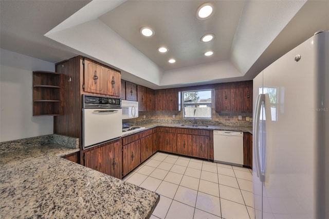 kitchen featuring sink, white appliances, light tile patterned floors, backsplash, and a tray ceiling