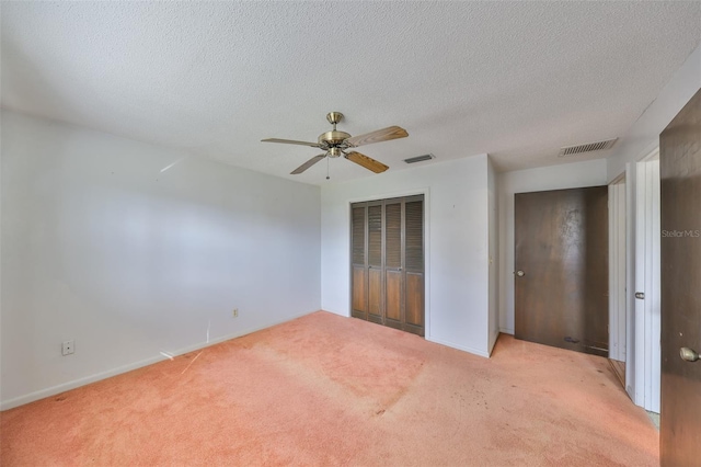 unfurnished bedroom featuring ceiling fan, a closet, light carpet, and a textured ceiling