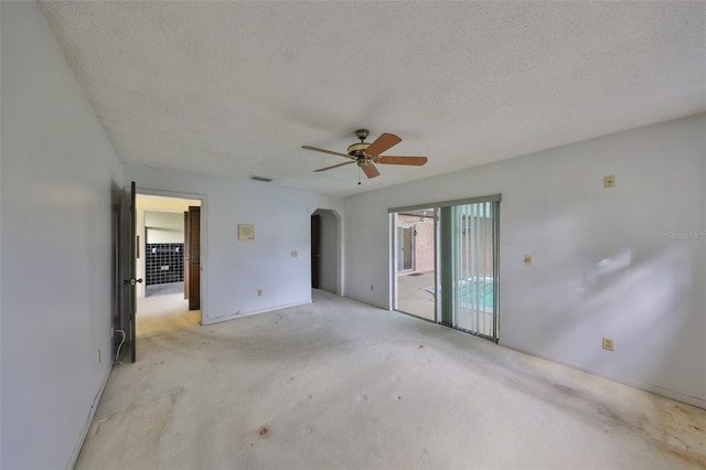 empty room with ceiling fan, light colored carpet, and a textured ceiling