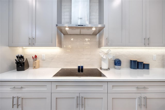 kitchen with black electric cooktop, wall chimney range hood, tasteful backsplash, and white cabinets