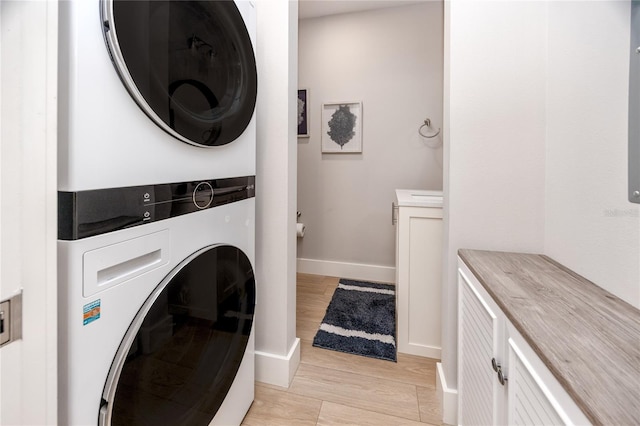 washroom with cabinets, stacked washer and clothes dryer, and light hardwood / wood-style floors