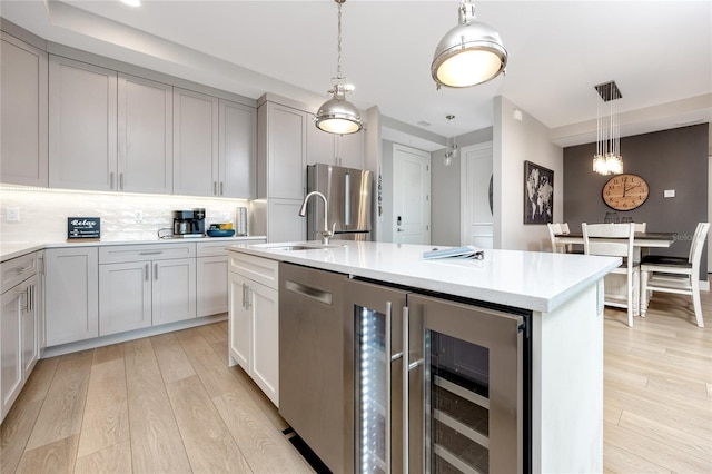 kitchen featuring decorative light fixtures, gray cabinets, stainless steel appliances, and an island with sink