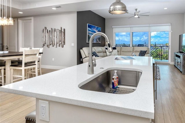 kitchen with hanging light fixtures, light stone countertops, a kitchen island with sink, and sink