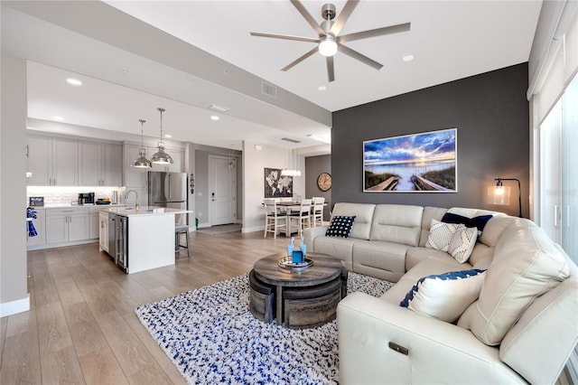 living room with sink, light hardwood / wood-style floors, and ceiling fan