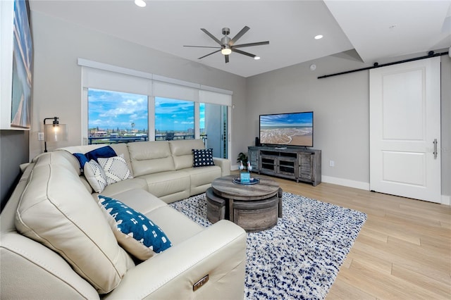 living room featuring ceiling fan, a barn door, and light hardwood / wood-style floors