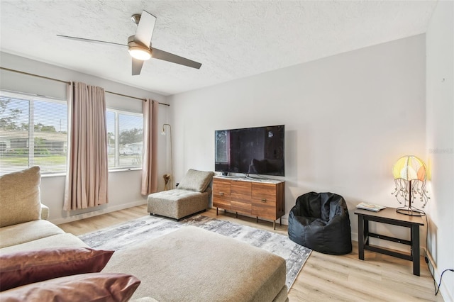 living room with ceiling fan, a textured ceiling, and light wood-type flooring