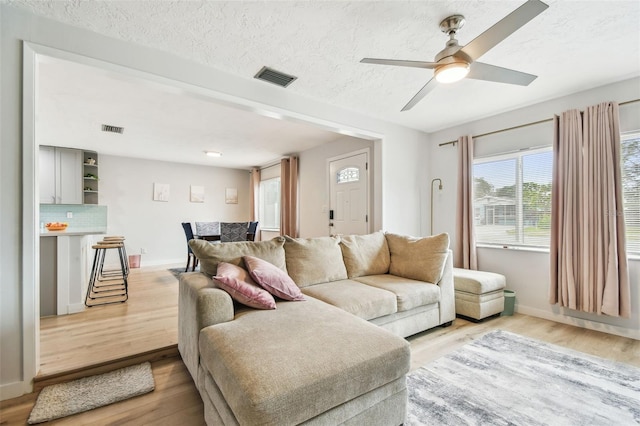 living room with a textured ceiling, light hardwood / wood-style floors, and ceiling fan