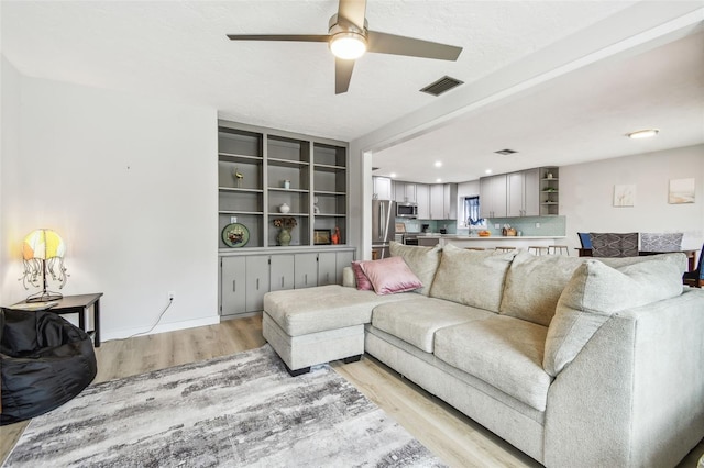 living room with ceiling fan, light wood-type flooring, and built in shelves