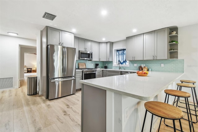 kitchen featuring a kitchen bar, gray cabinetry, light wood-type flooring, appliances with stainless steel finishes, and kitchen peninsula