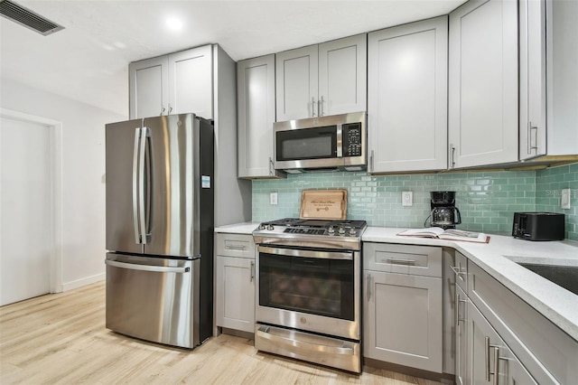 kitchen with gray cabinetry, decorative backsplash, light hardwood / wood-style floors, and appliances with stainless steel finishes